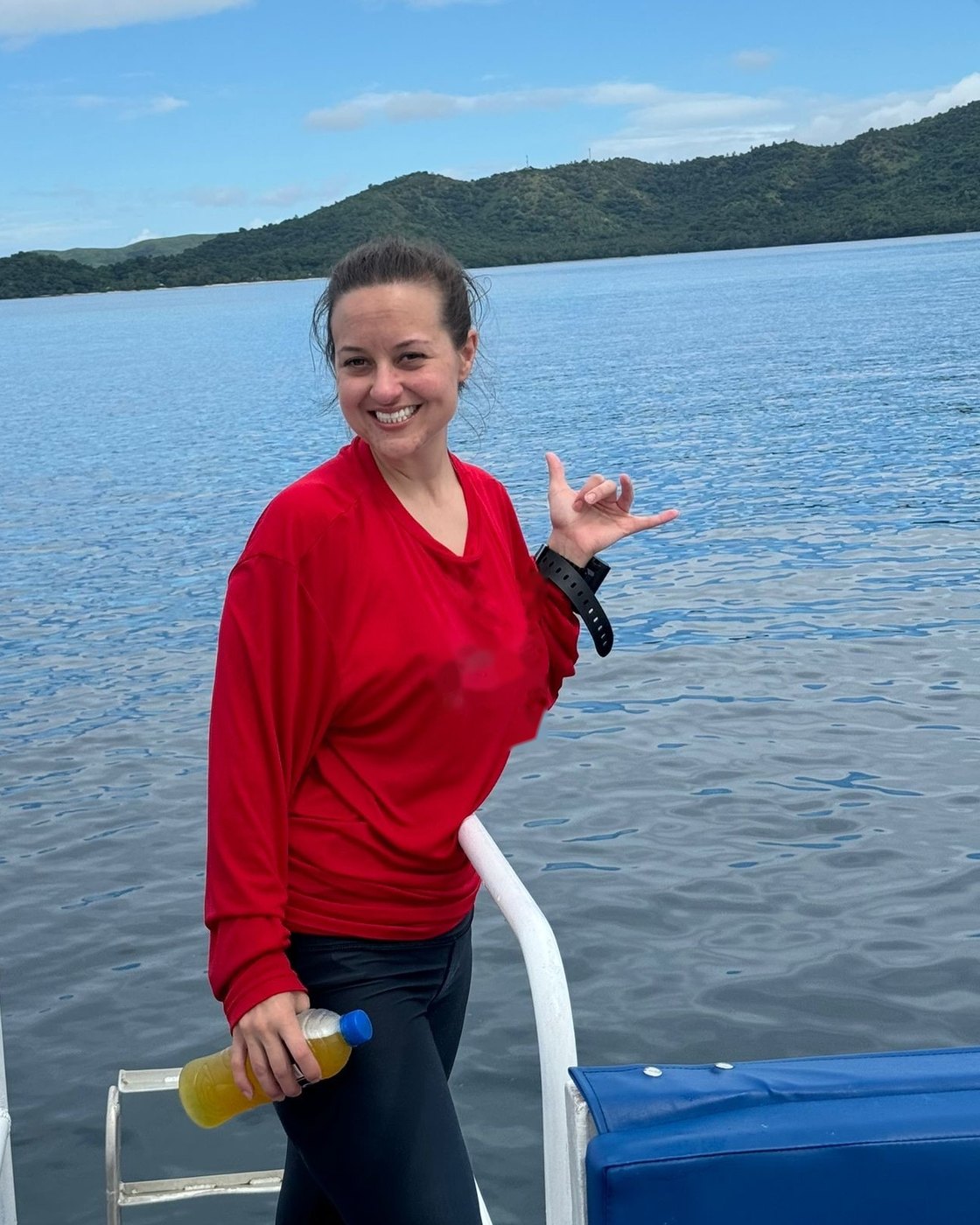 Allie on the dive boat off Taveuni, Fiji, giving a shaka with the island behind her