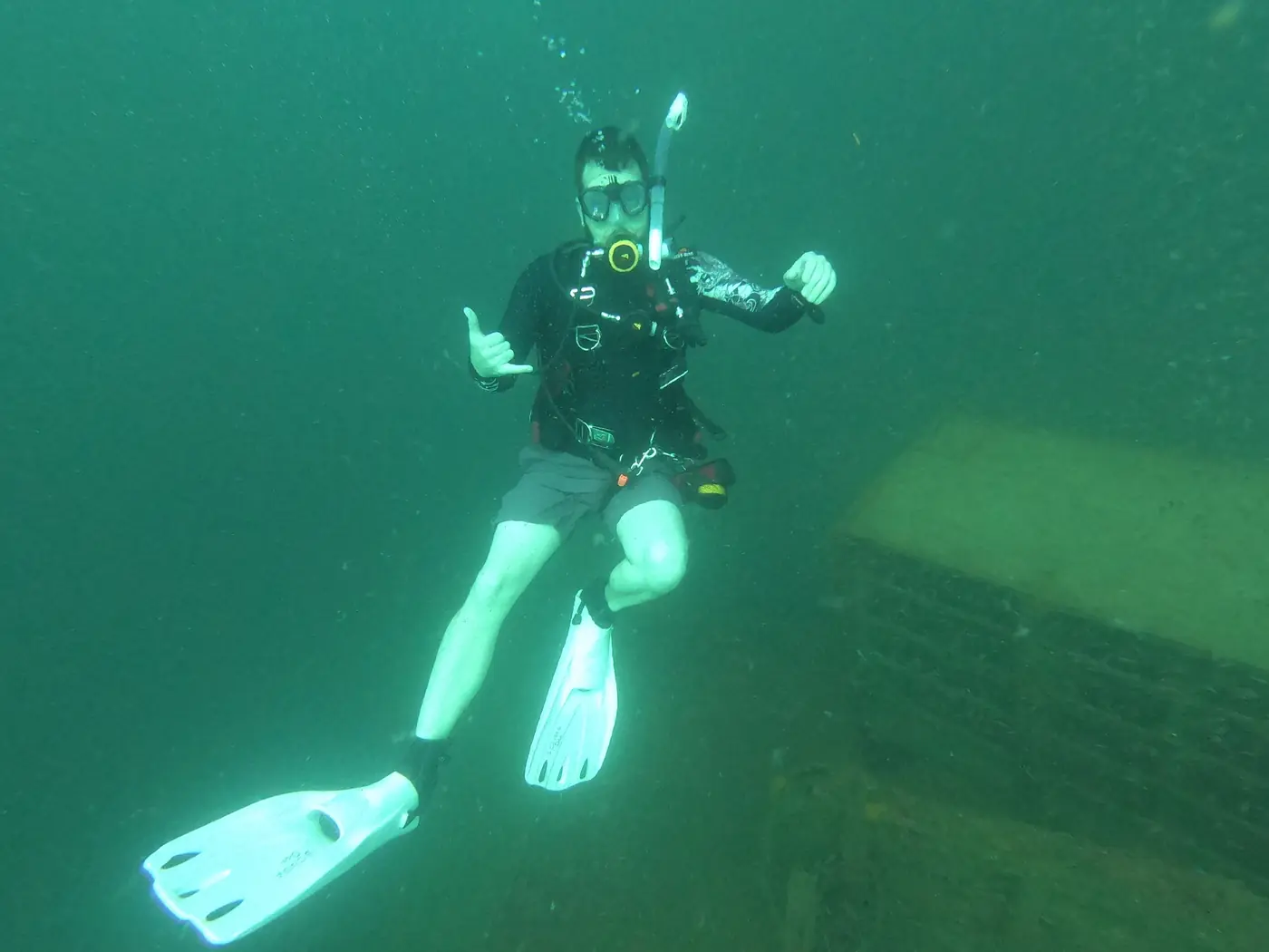 Eric giving a shaka in green Gulf water beside a sunken structure